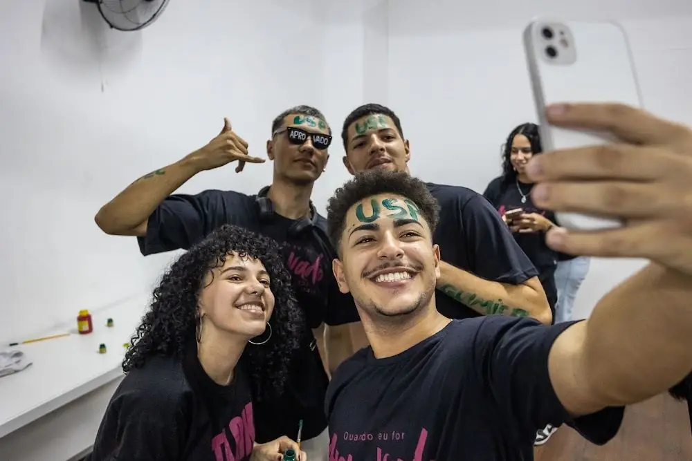 Alunos aprovados tirando selfie com o nome da faculdade escrito na testa
