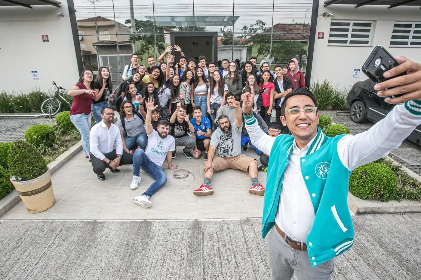 Marco Ohmori tirando selfie com alunos em frente a uma unidade da Ohmori