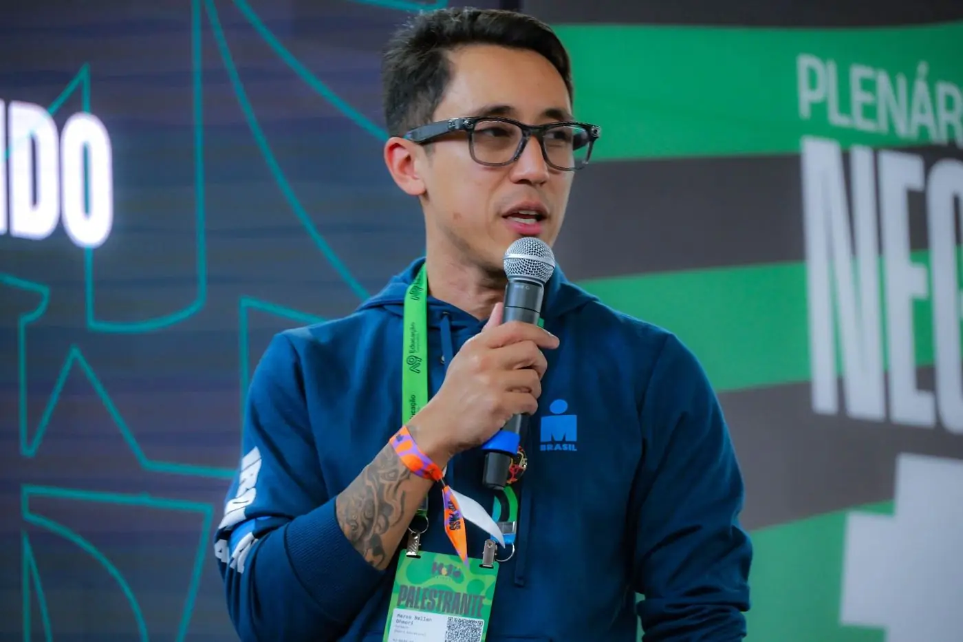 Marco Ohmori falando ao microfone no palco de um evento